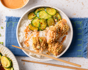 Salmon nuggets on top of rice in bowl with cucumber salad and drizzled with homemade bang bang sauce.
