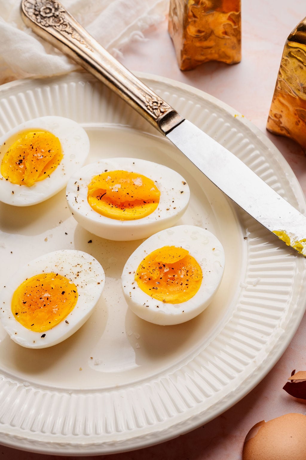 Soft and medium hard boiled egg halves sprinkled with salt and black pepper on a white plate with a butter knife alongside.