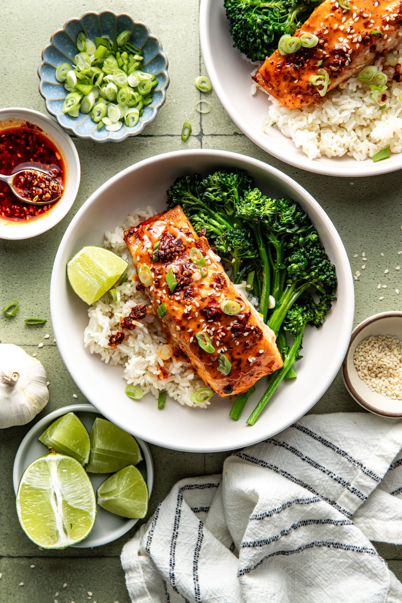 Chili crisp salmon plated in a bowl with broccolini, rice and a wedge of lime.