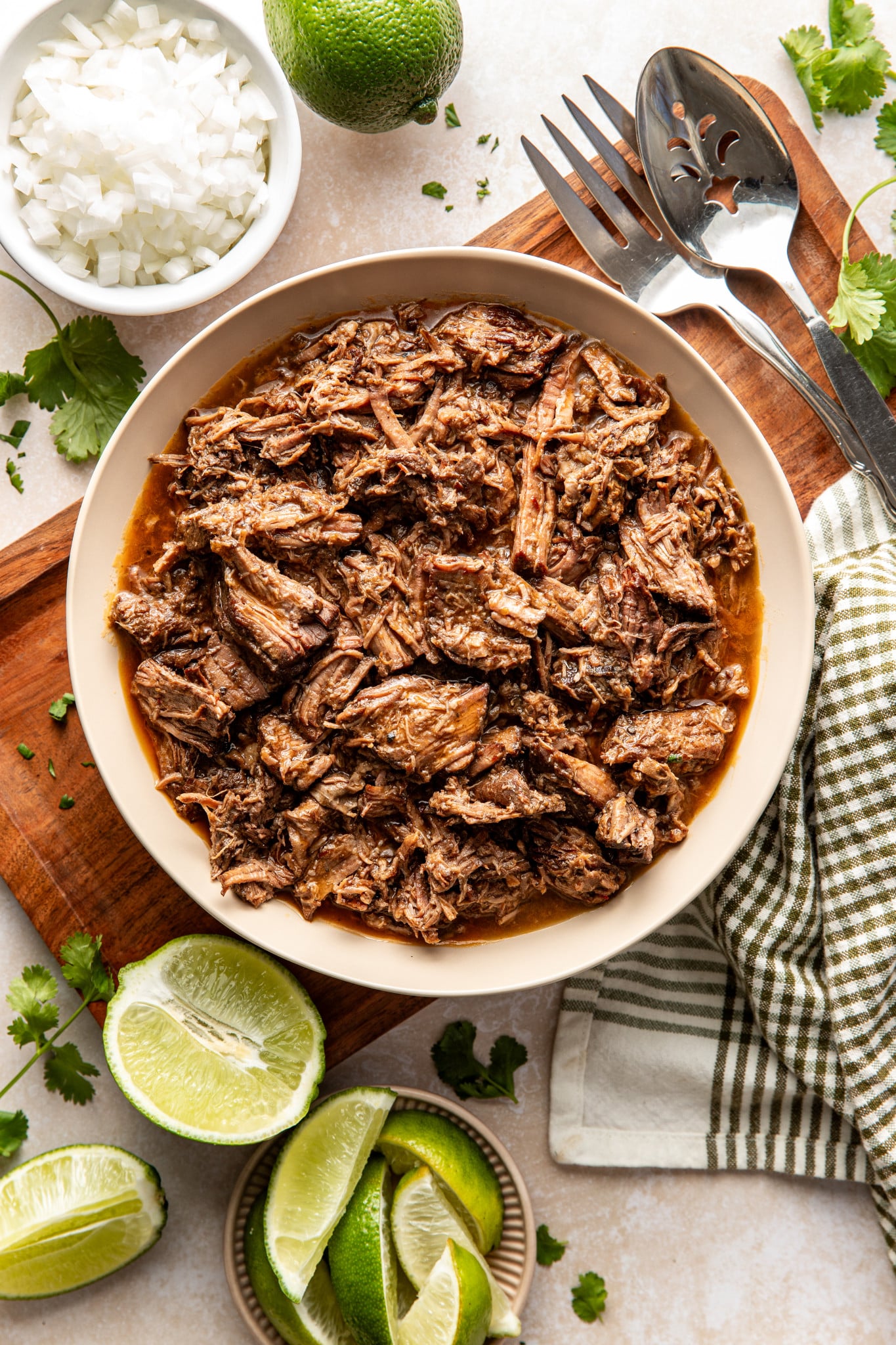 Shredded beef barbacoa in a bowl on top of a wooden serving tray.