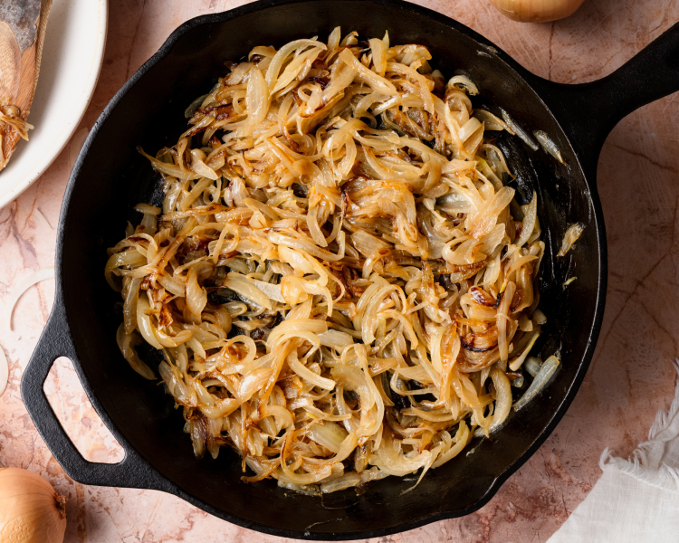 Onions starting to cook down in a cast-iron pan halfway through cooking them to caramelized.