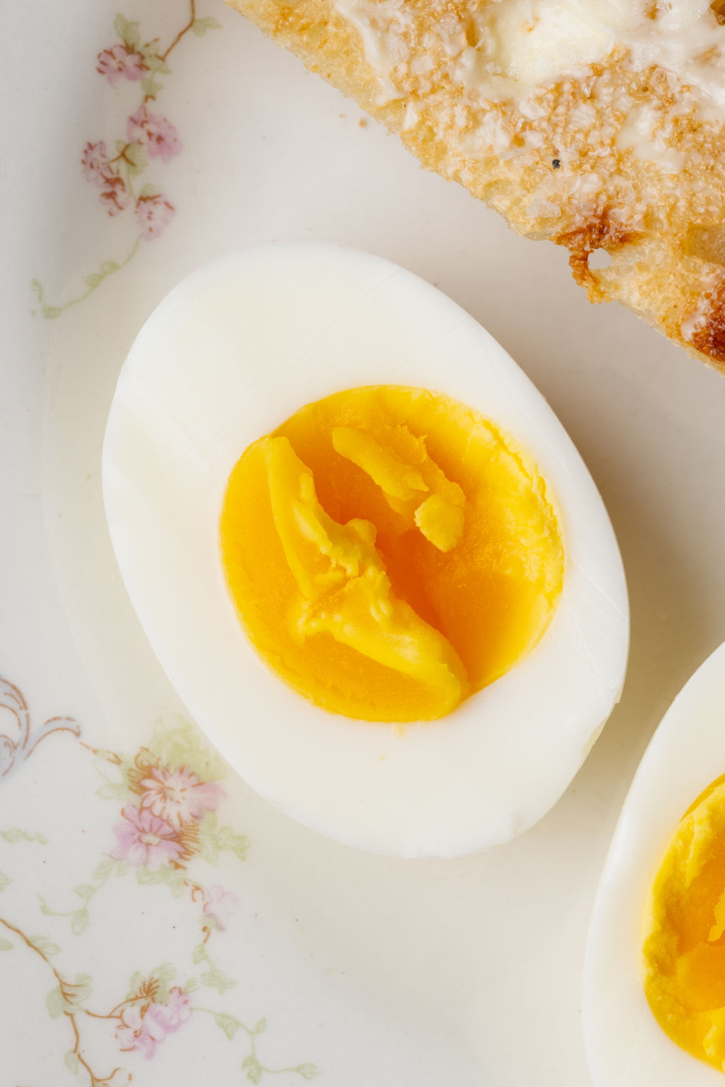Close-up of a sliced hard boiled egg with a slightly jammy golden yolk on a floral plate.