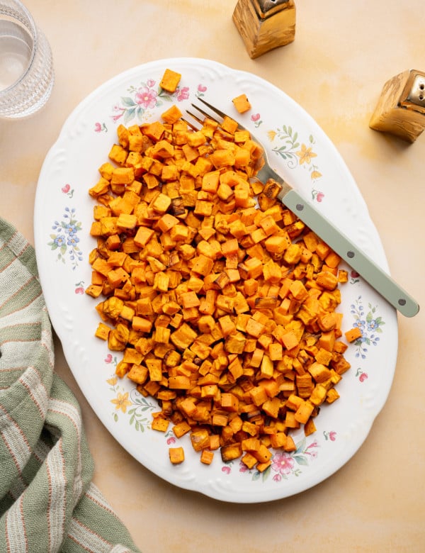 Cooked sweet potatoes on a large oval serving plate with fork on the right side.