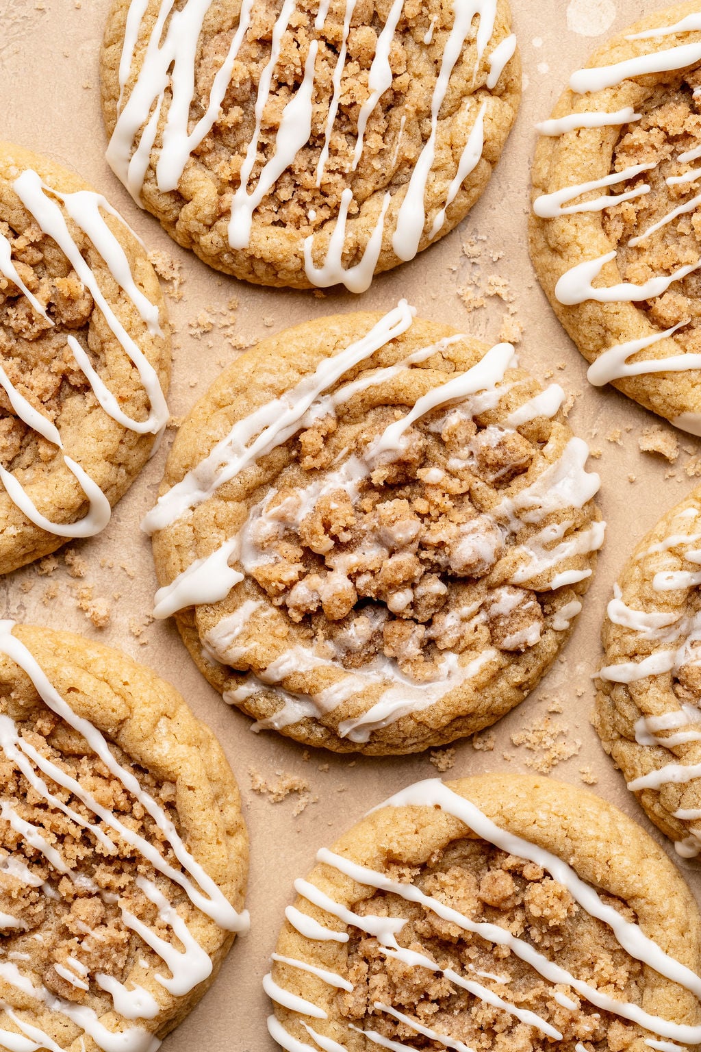 Overhead view of multiple coffee cake cookies arranged on parchment paper, each topped with crumb streusel and finished with a light white glaze drizzle.