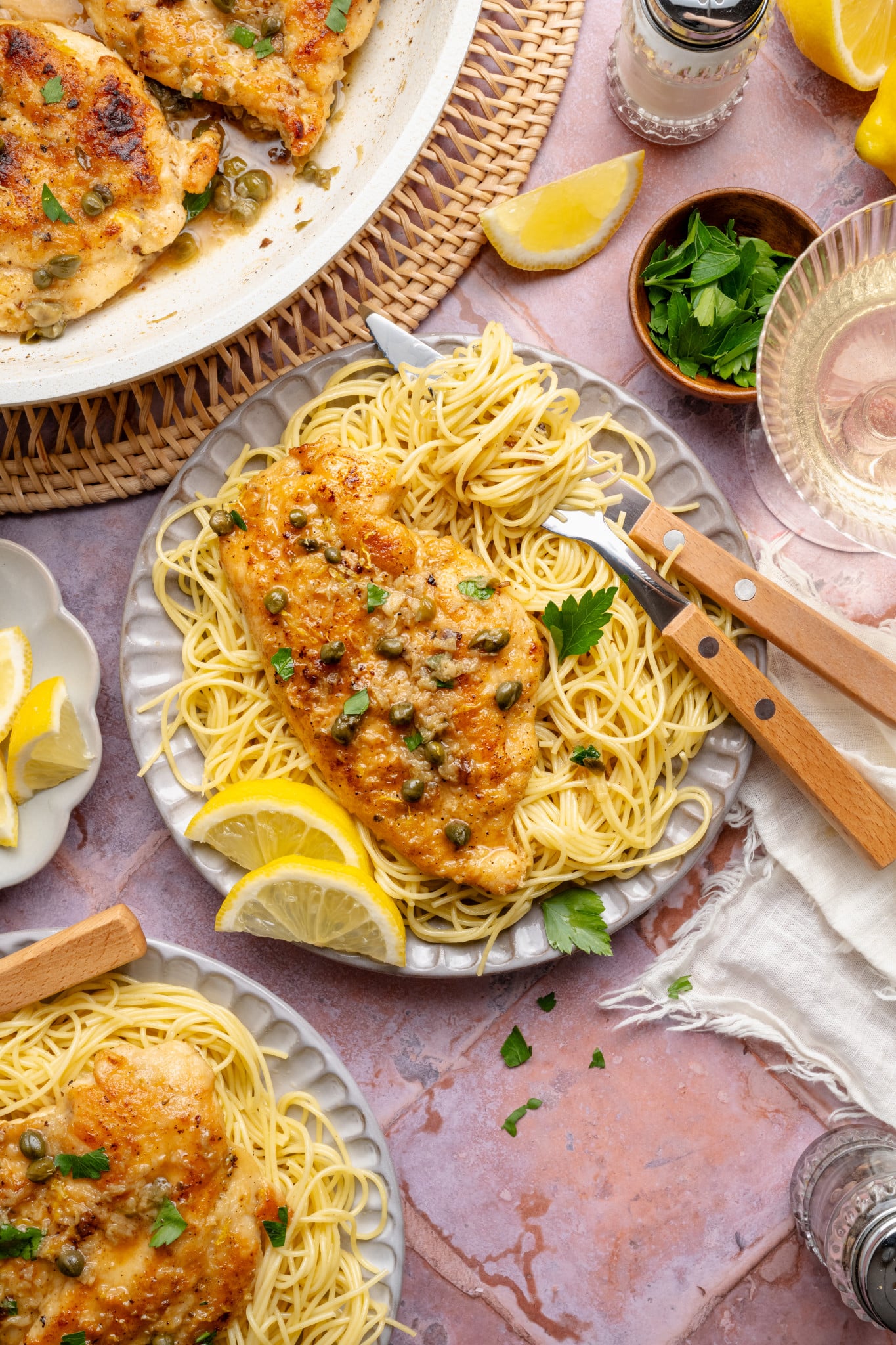 Chicken piccata served on top of spaghetti pasta on a plate with fork and knife.