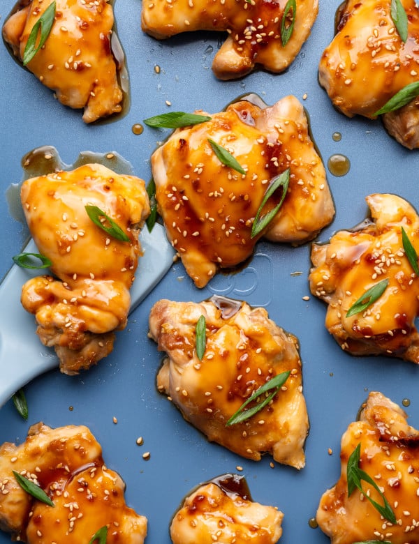 Oven baked teriyaki chicken thighs on a baking tray garnished with green onions and sesame seeds.