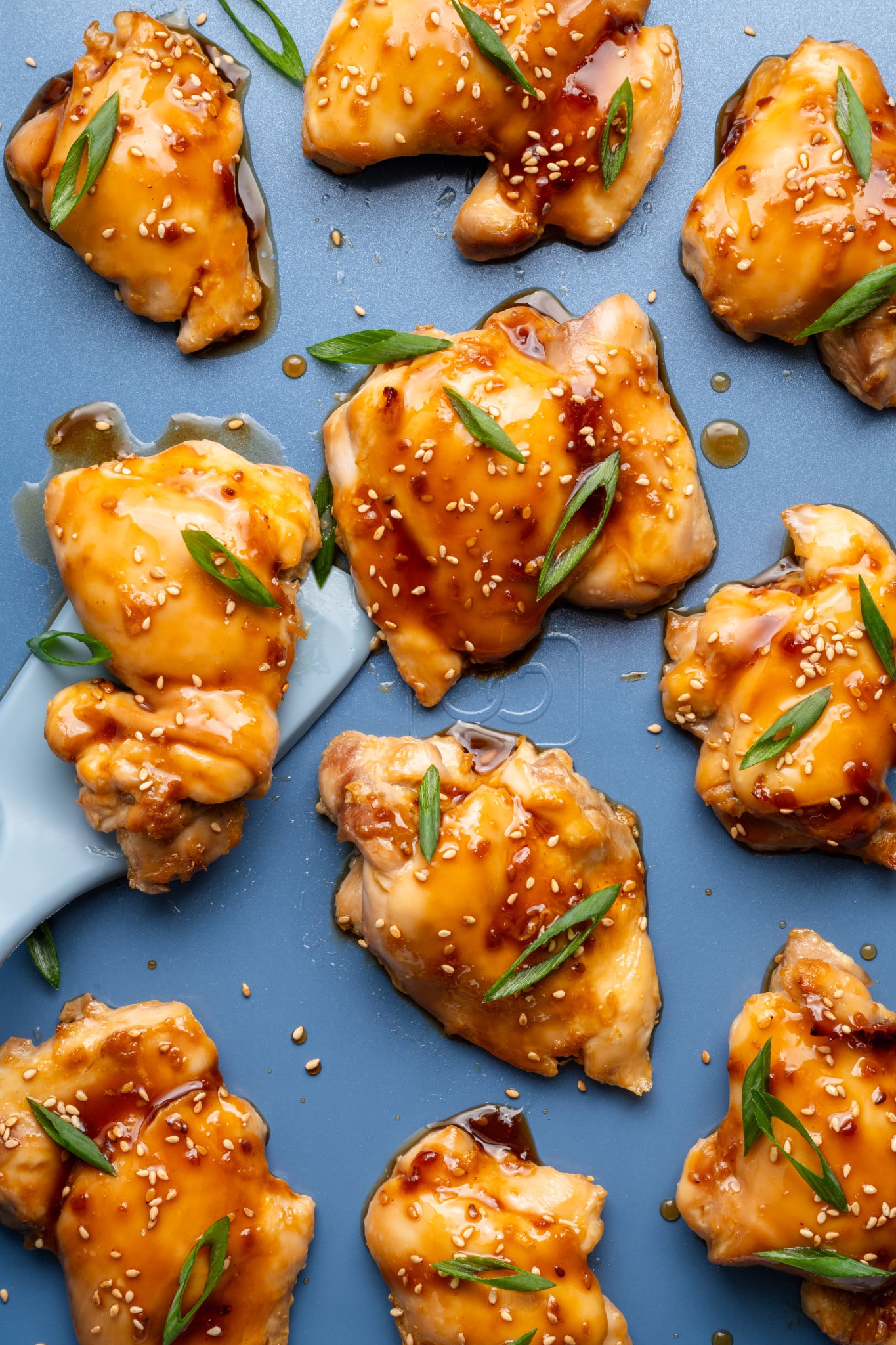 Oven baked teriyaki chicken thighs on a baking tray garnished with green onions and sesame seeds.