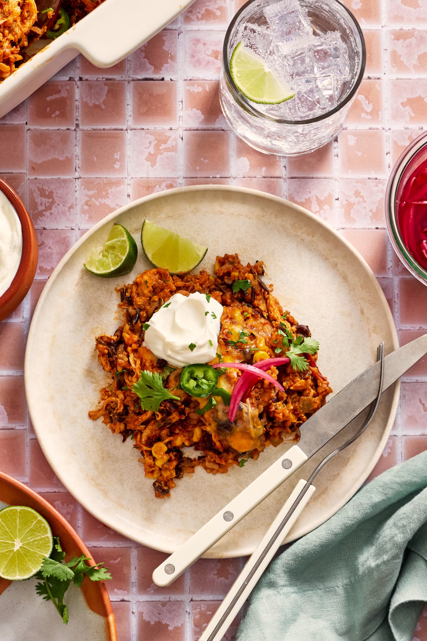 Chicken and rice enchilada casserole on a plate garnished with pickled red onions, jalapenos, sour cream and cilantro.