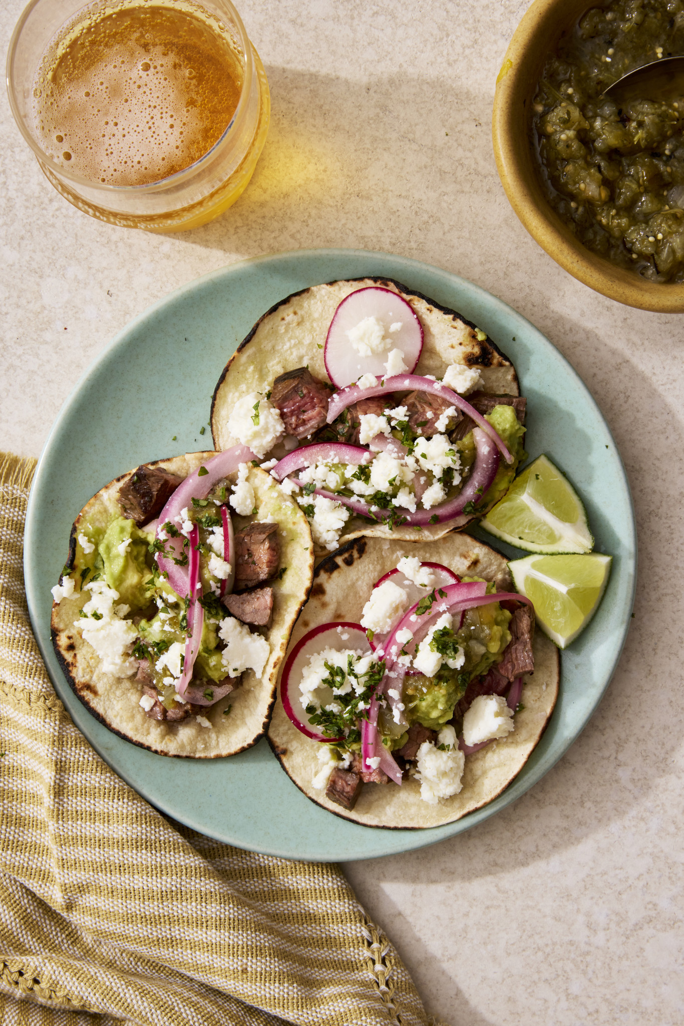 Three carne asada tacos on a blue plate with toppings.