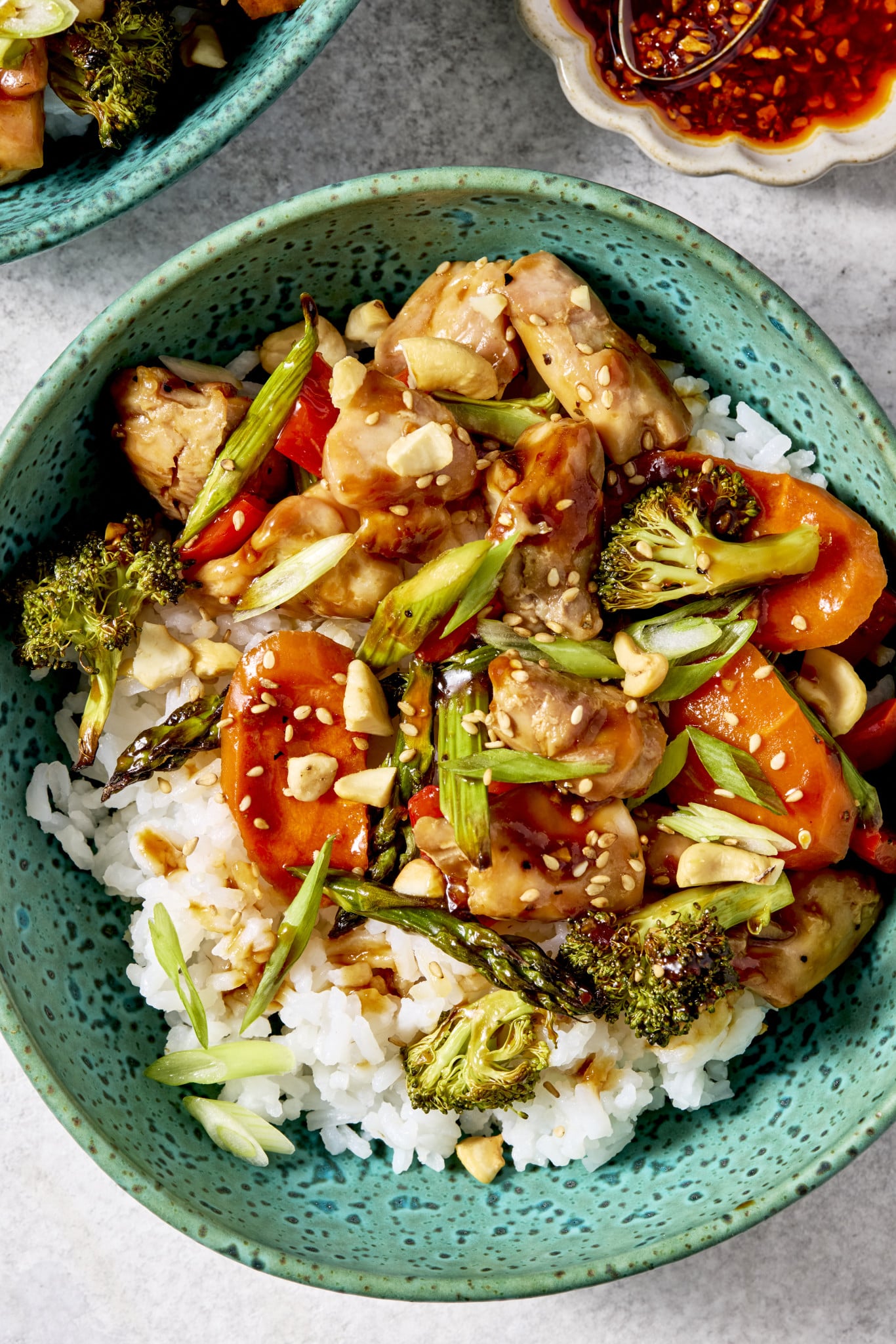Sheet pan sesame chicken and veggies served in a bowl with on top of rice and garnished with green onions and sesame seeds.