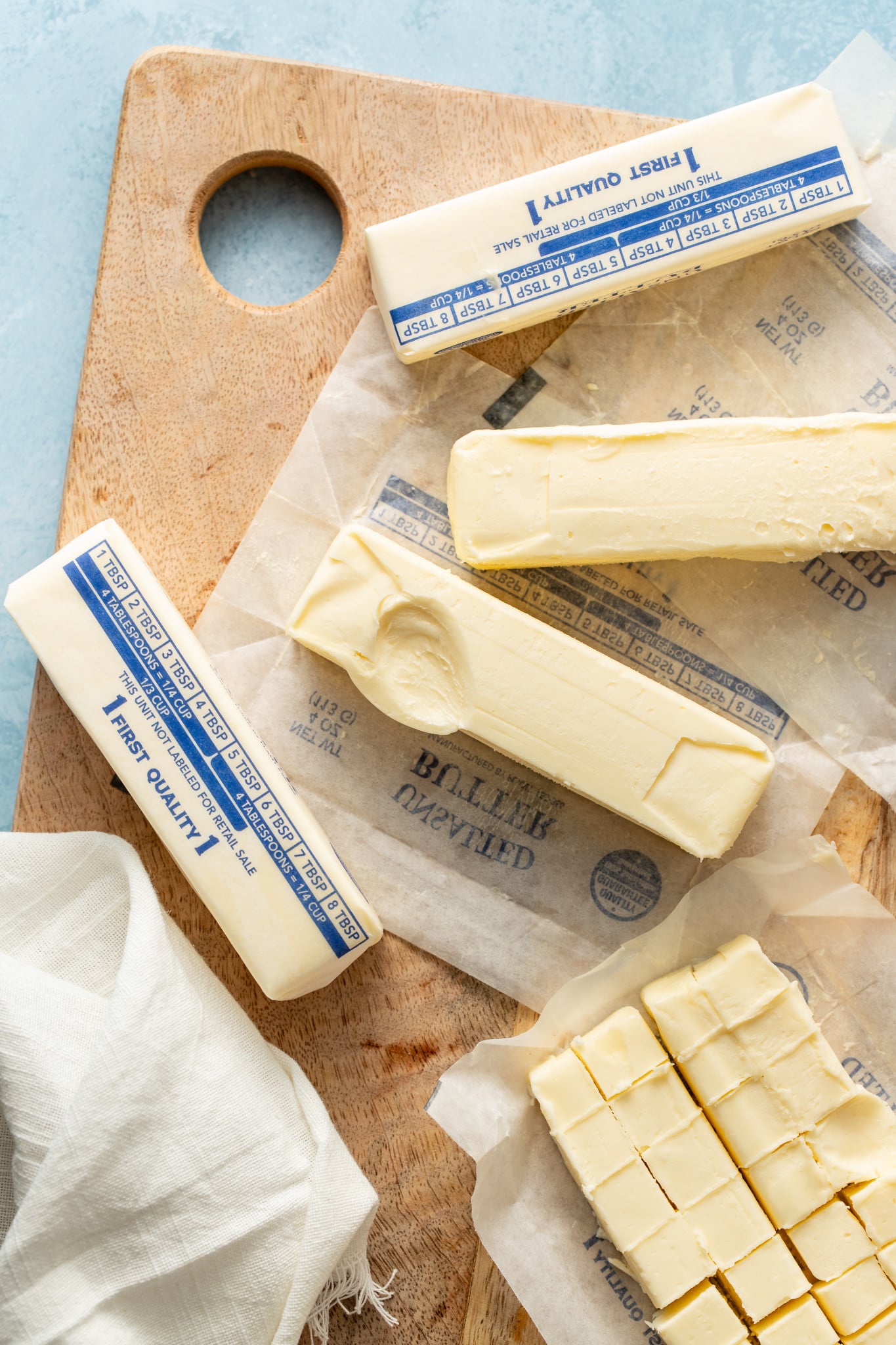 Several sticks of butter softened on wood cutting board with one stick showing indention.