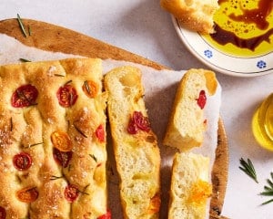 Finished homemade focaccia topped with cherry tomatoes, fresh rosemary, flaky sea salt, and olive oil, served with olive oil and balsamic vinegar for dipping.
