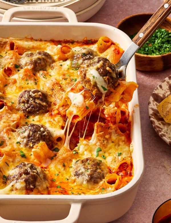 Fork scooping out pasta and meatball from bake in casserole dish.