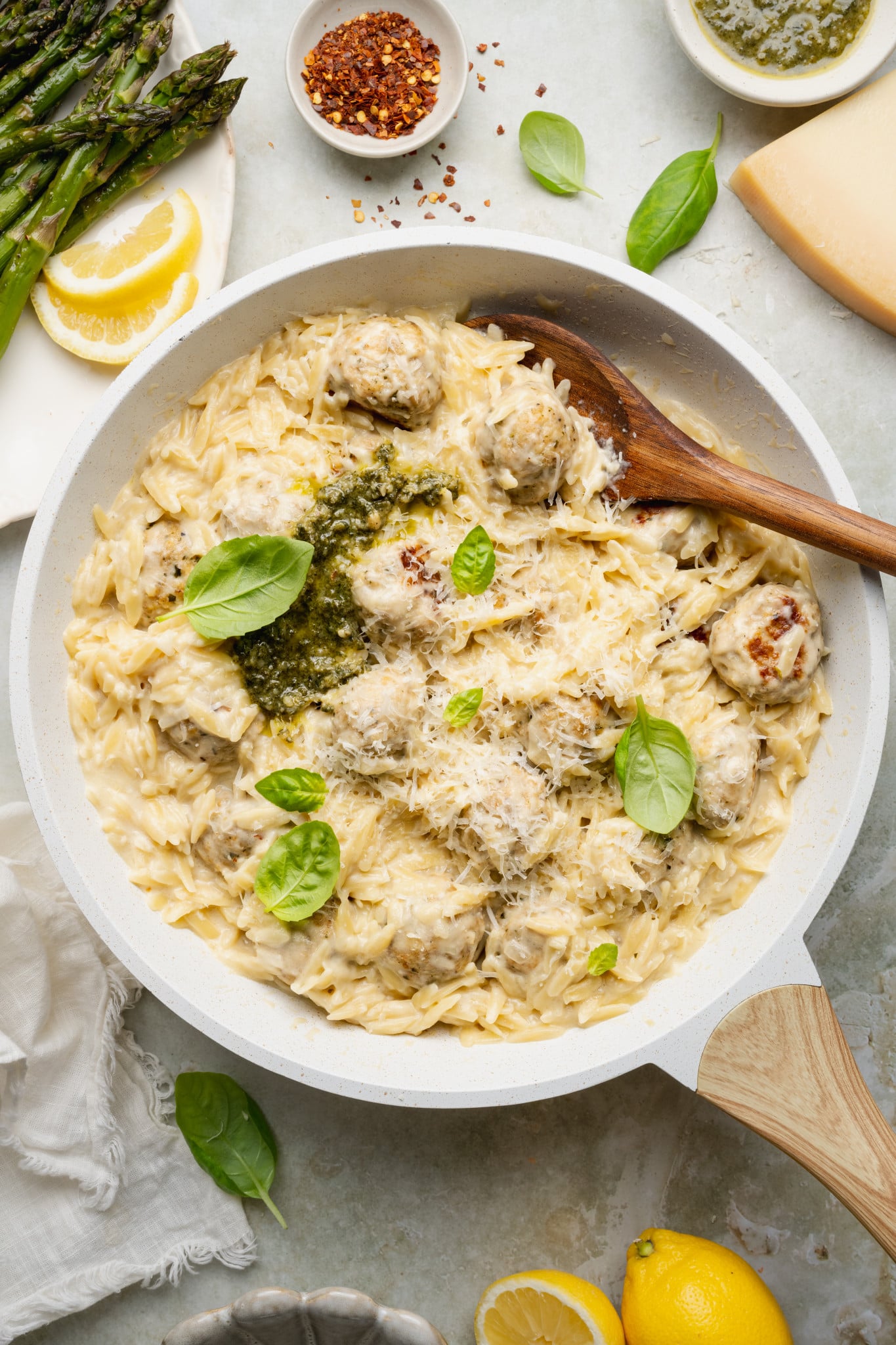 Pesto chicken meatballs and orzo cooked in skillet and topped with extra basil, pesto and parmesan cheese.