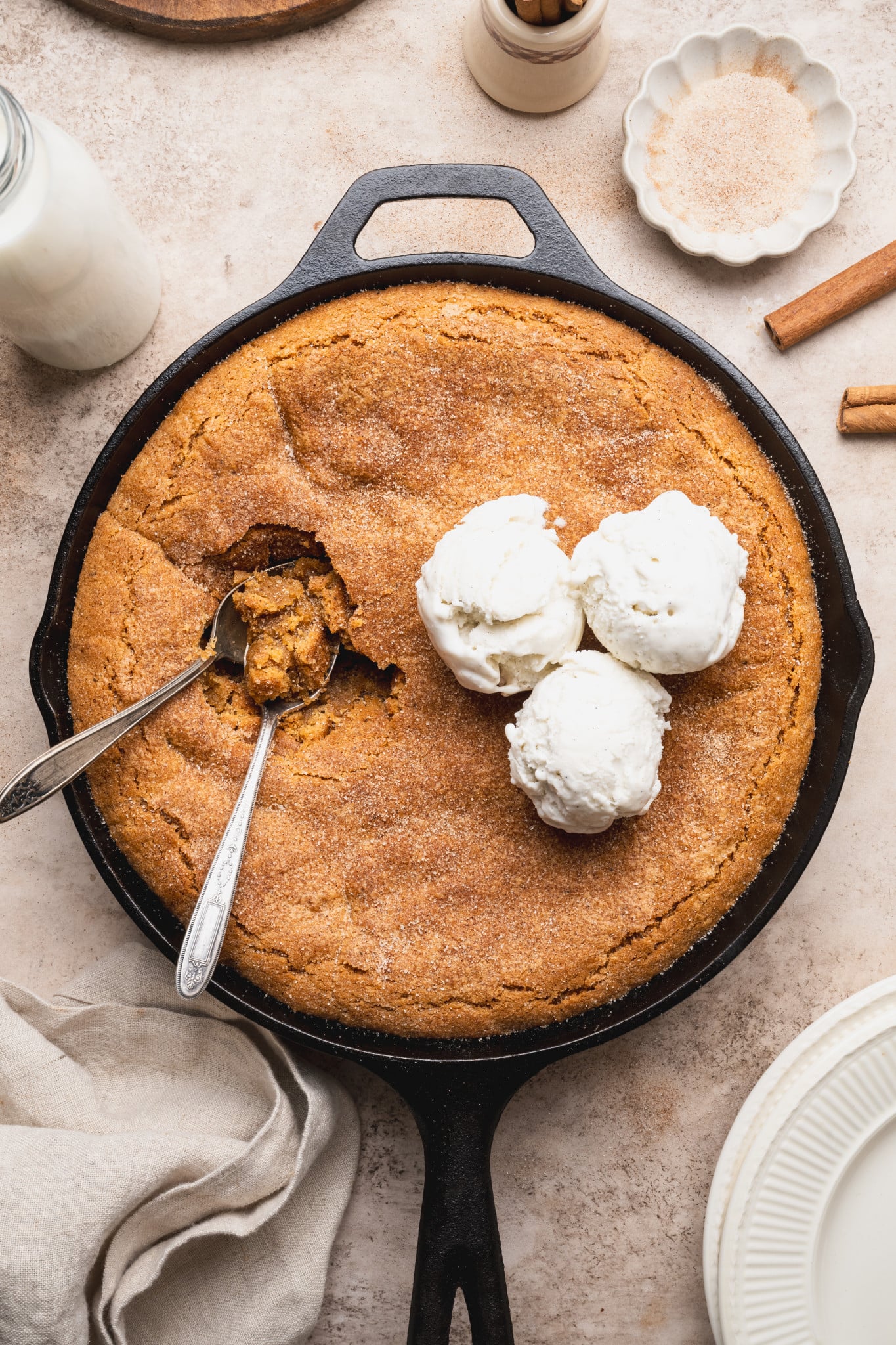 Snickerdoodle cookie skillet topped with three scoops of vanilla ice cream with two spoons digging in.