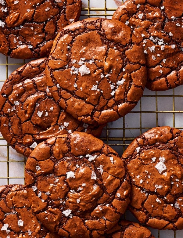 Crackly top brownie cookies piled on a cooling rack and sprinkled with flaky salt.