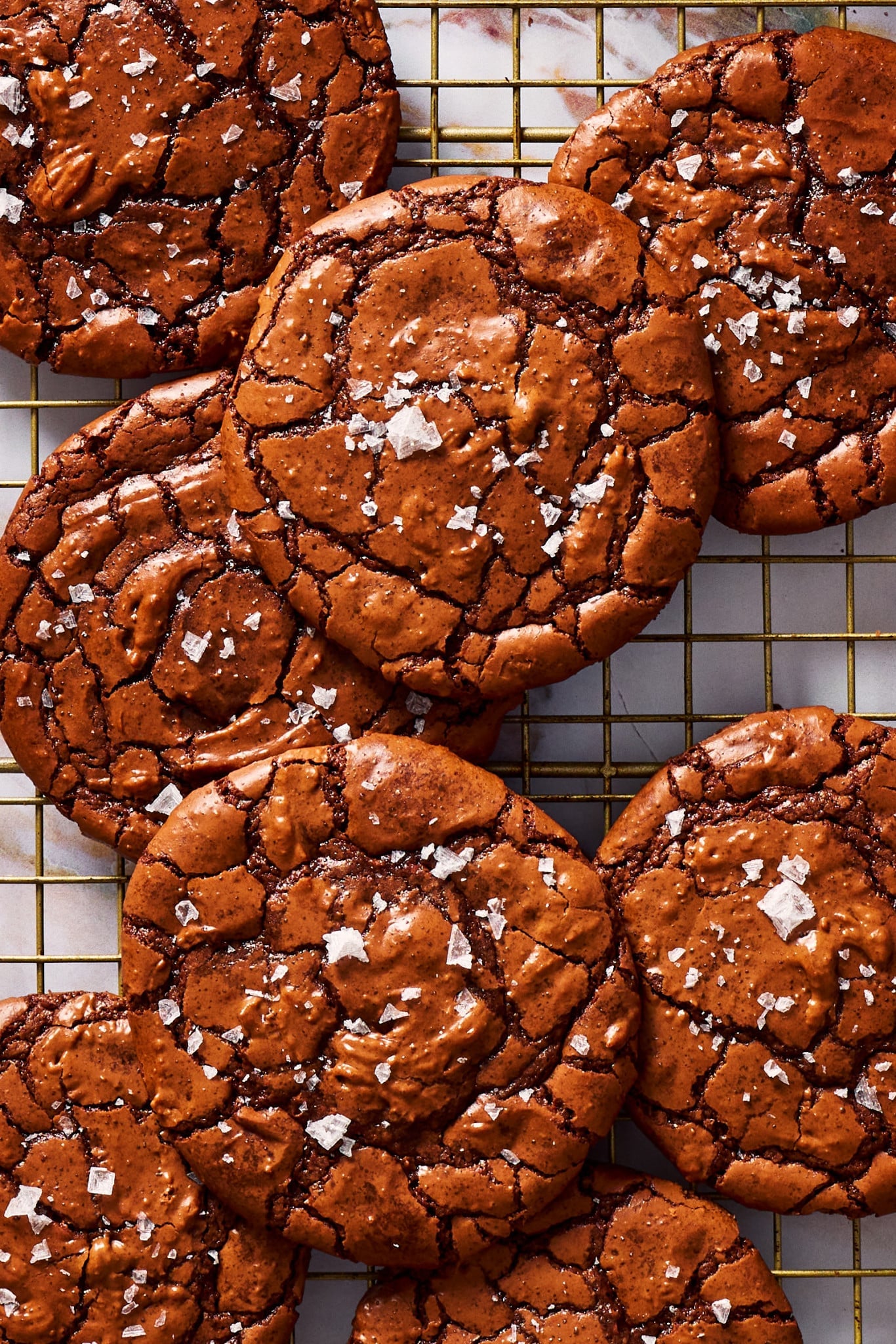 Crackly top brownie cookies piled on a cooling rack and sprinkled with flaky salt.