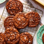 Crackly top brownie cookies on top of cooling rack sprinkled with flaky salt.