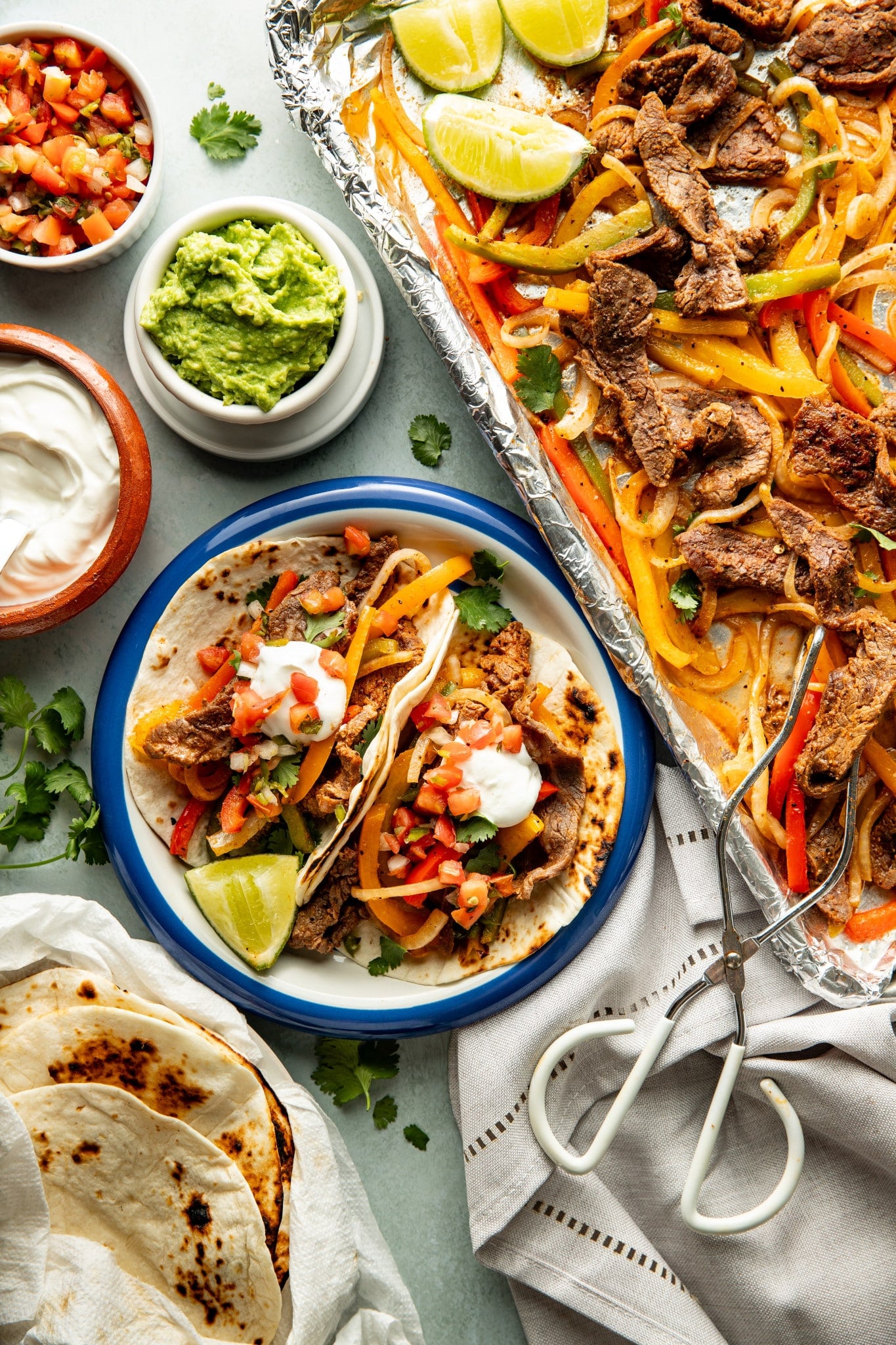 Two tortillas filled with steak fajitas on a plate and topped with sour cream and pico de gallo.