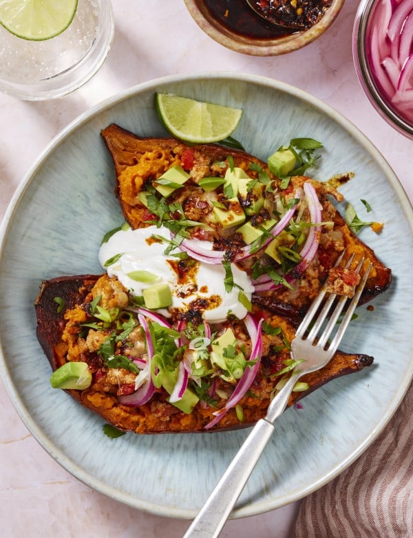 Two sweet potato halves topped with ground turkey, avocado, sour cream, pickled red onions and cilantro on a plate with a fork.