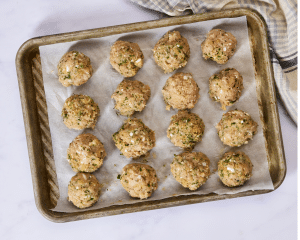 Meatballs scooped and rolled then placed on parchment-lined baking sheet.