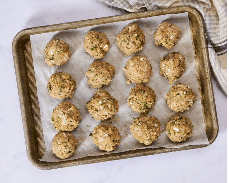 Meatballs scooped and rolled then placed on parchment-lined baking sheet.
