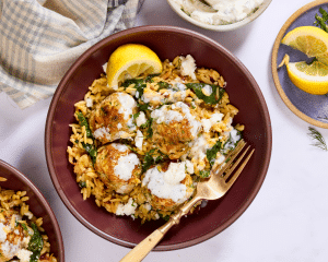 Cooked meatballs and orzo served in a bowl then topped with tzatziki and a lemon wedge.